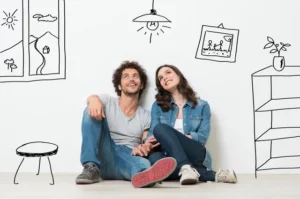 A man and woman sitting on the ground with drawings of their home.
